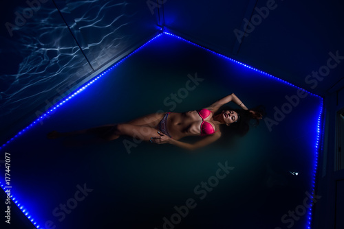 Beautiful tanned woman in pink swimwear relaxing in swimming pool spa