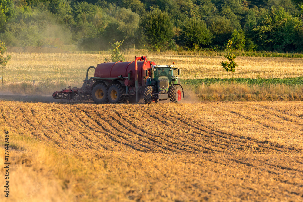Fototapeta premium Grüner Traktor mit rotem Anhänger biegt in ein Feld ein, um es zu düngen