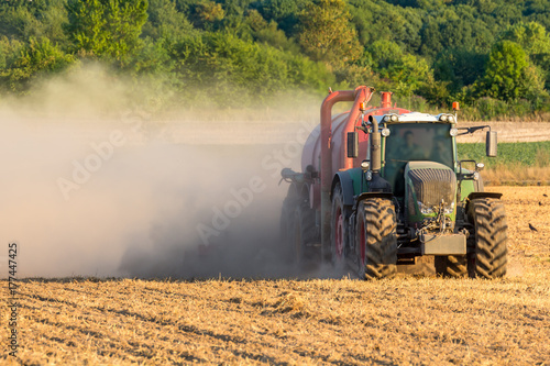 Grüner Traktor mit rotem Anhänger wirbelt eine Staubwolke auf dem Feld auf, closeup © levelupart