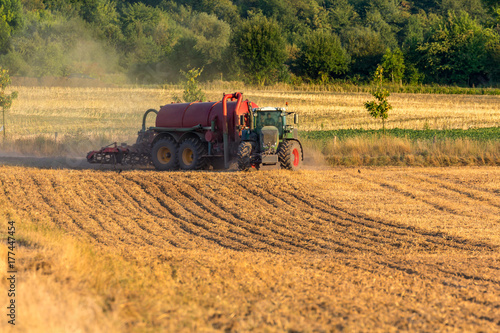 Grüner Traktor mit rotem Anhänger biegt in ein Feld ein, um es zu düngen