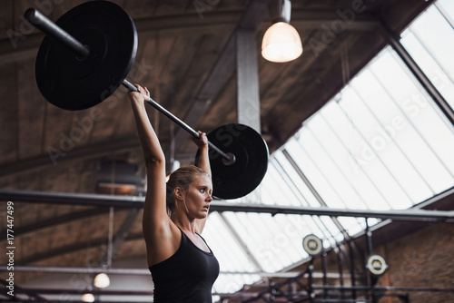 Fit woman lifting barbells over her head in a gym
