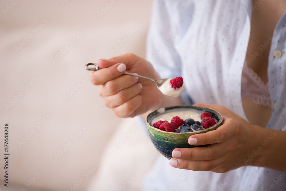 Woman sitting on a sofa and eating organic yogurt with blueberries and raspberries. Healthy breakfast at home. Woman sitting on a sofa and eating organic yogurt with blueberries and raspberries. Healthy breakfast at home.