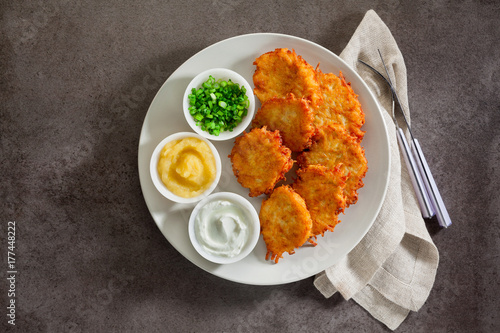 Potato pancakes, latkes or boxty and sauces from sour cream, yogurt, apple sauce and finely chopped green onion on grey stone background