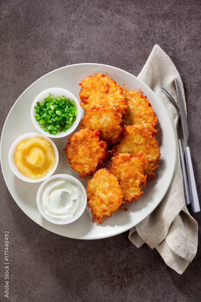Potato pancakes, latkes or boxty and sauces from sour cream, yogurt, apple sauce and finely chopped green onion on grey stone background Potato pancakes, latkes or boxty and sauces from sour cream, yogurt, apple sauce and finely chopped green onion on grey stone background