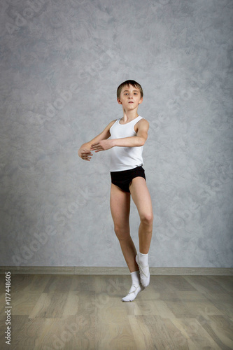Little ballet caucasian boy dancing in a studio in white shirt and black underpants ballet uniform. Full-length portrait.