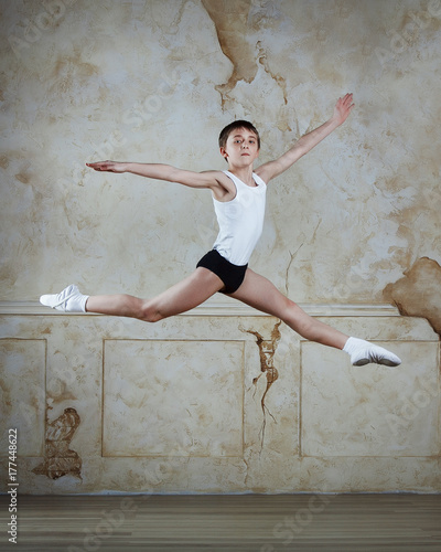 Little ballet caucasian boy dancing in a studio in white shirt and black underpants ballet uniform. Full-length portrait.