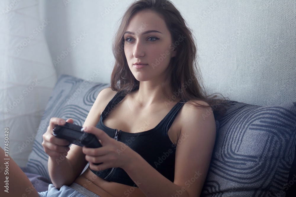 Attractive brunette caucasian woman in home wear, sit at the bed, play video-games with game-pad, look at TV screen with different emotions Attractive brunette caucasian woman in home wear, sit at the bed, play video-games with game-pad, look at TV screen with different emotions