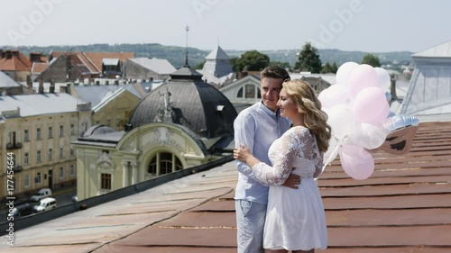 Couple holding some ballons on the rooftoop hugging and looking at city photo