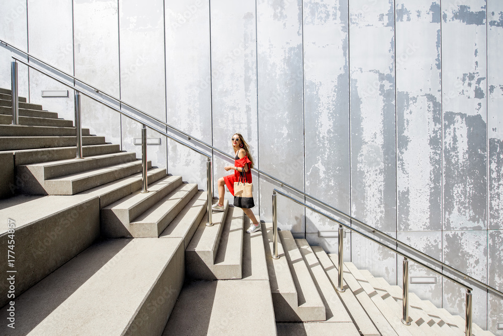 Business woman in red dress on the big stairway on the grey wall background
