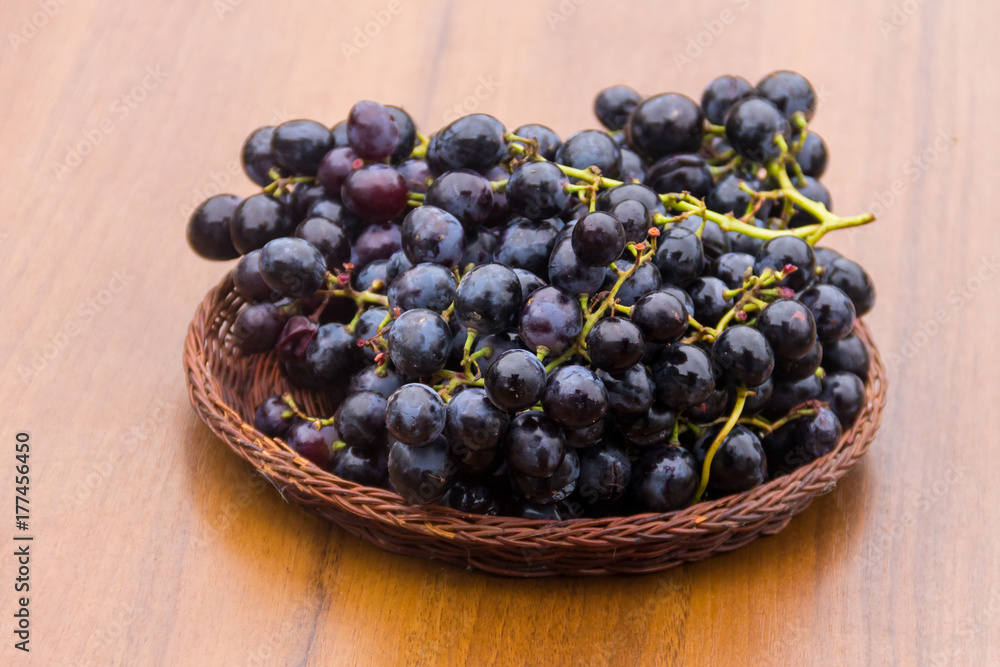 Ripe grapes in wicker basket on wooden table Ripe grapes in wicker basket on wooden table