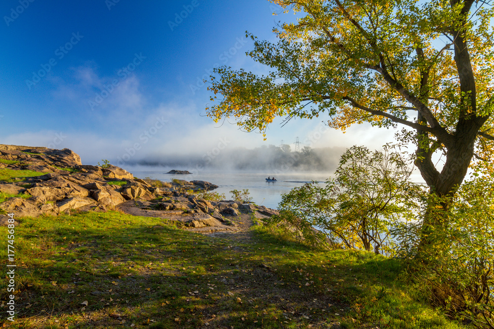 Beautiful autumn morning landscape with fog over the Dnieper river and fishermen boat sailing Beautiful autumn morning landscape with fog over the Dnieper river and fishermen boat sailing