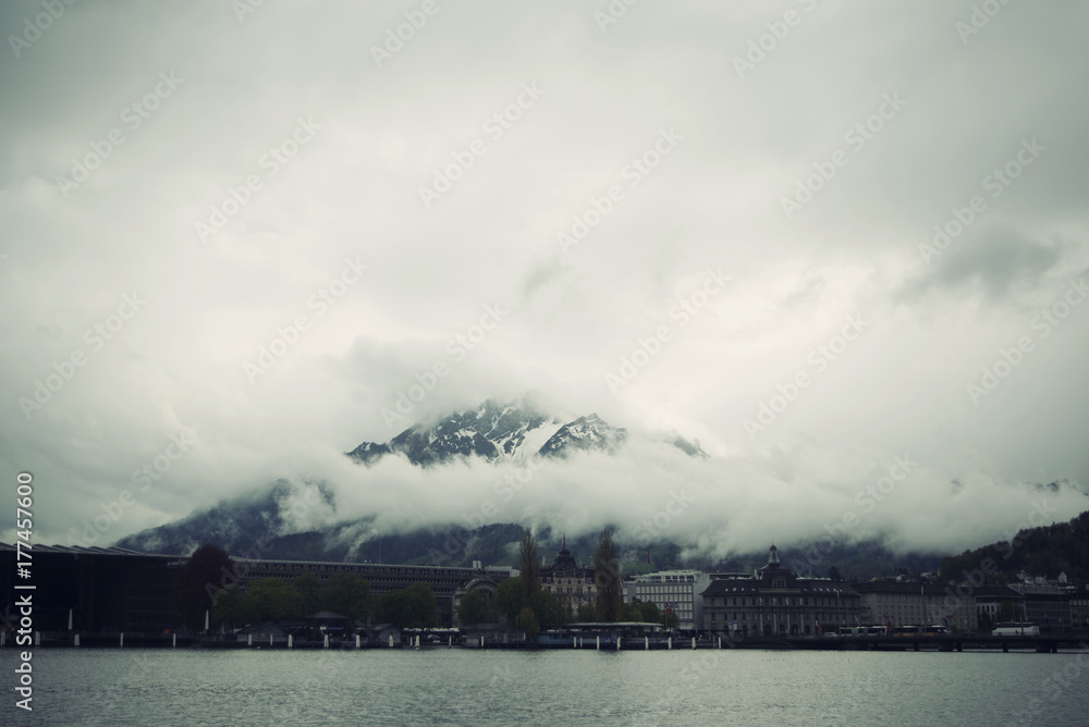 Paisaje invernal suizo con las montañas de Los Alpes cubiertas de niebla densa blanca con edificios en primer término.