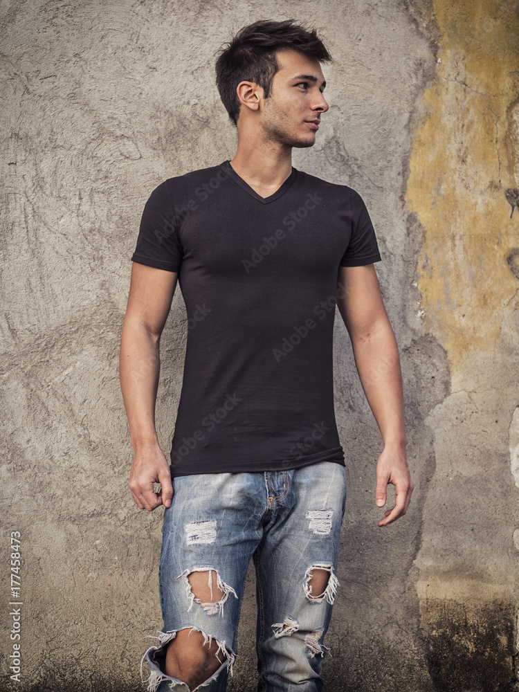 Smiling young man standing against concrete wall. Looking away Smiling young man standing against concrete wall. Looking away