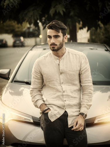 Portrait of young bearded man leaning on his new stylish polished car, outdoor © starsstudio