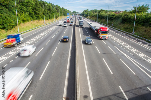 An aerial photograph of a busy motorway in the UK with three lanes and a junction and traffic including cars and trucks speeding by with blurred motion. photo