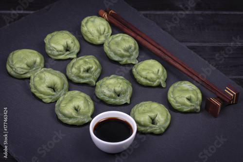Ukrainian and Russian dishes - green dumplings with beef meat or mashed potatoes or cottage cheese in the dough, together with spirulina on a black slate background