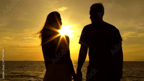 Romantic couple Sitting on the Pier at colorful sunset on background. Young Couple at the Sea of Tropical Island