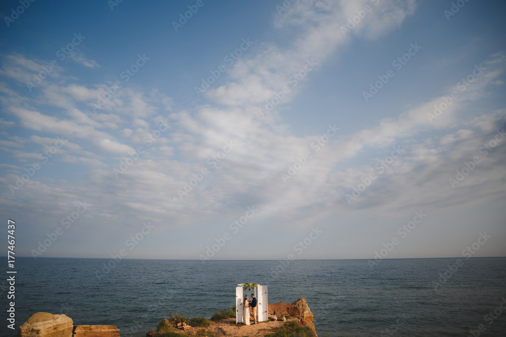 Outdoor beach wedding ceremony near the ocean, wedding couple are standing near the wedding altar on rock above the ocean