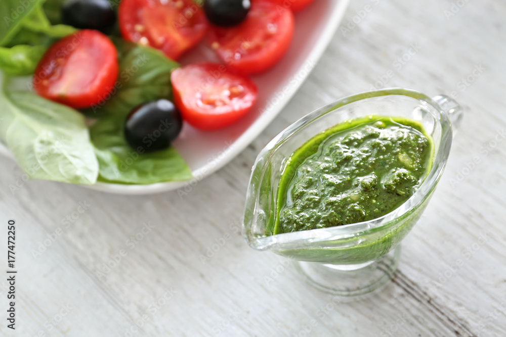 Obraz premium Gravy boat with basil pesto sauce on wooden table