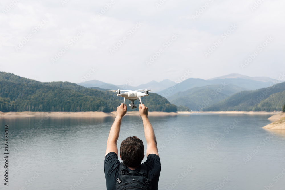 Man is holding white drone near Lake Vidraru at Fagaras Mountains. Romania Man is holding white drone near Lake Vidraru at Fagaras Mountains. Romania