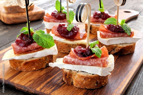 Holiday crostini appetizers with cranberry sauce, brie, salami, and mint on a wooden server photo