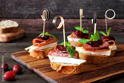Photography Holiday crostini skewers with cranberry sauce, brie, salami, and mint on a woode