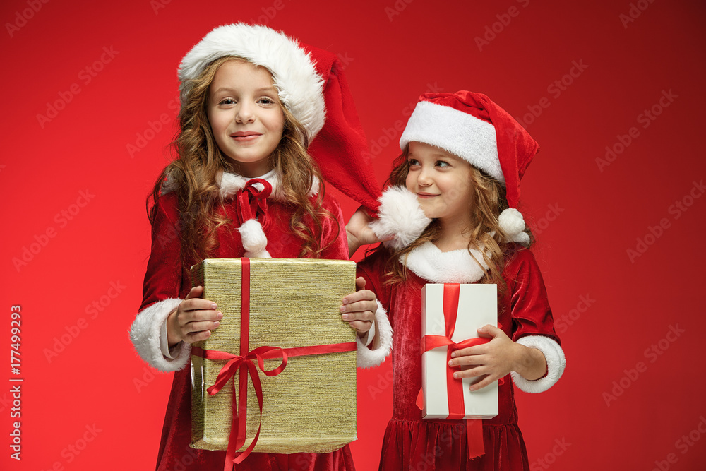 Two happy girls in santa claus hats with gift boxes at studio Two happy girls in santa claus hats with gift boxes at studio