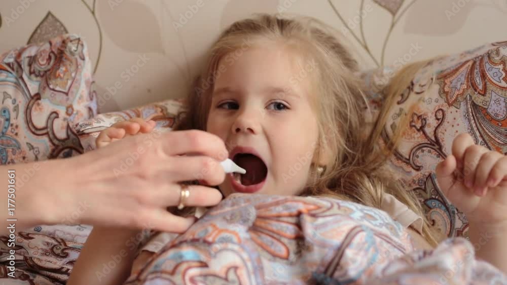 Sick little girl lying in bed and mother checking temperature putting thermometer in her mouth Sick little girl lying in bed and mother checking temperature putting thermometer in her mouth