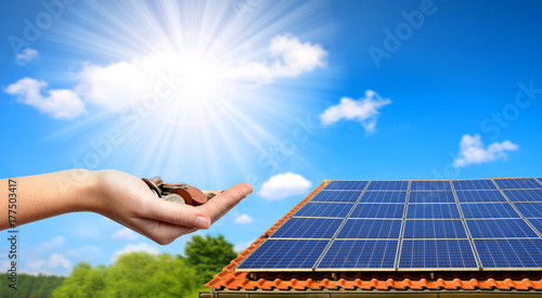 Solar panel on the roof of the house and coins in hand. The concept of money saving and clean energy.