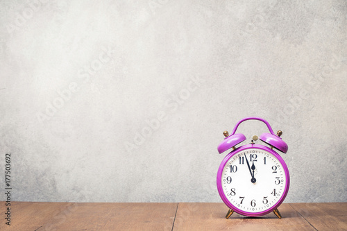 Old retro purple alarm clock on oak wooden table front concrete wall background. Vintage style filtered photo