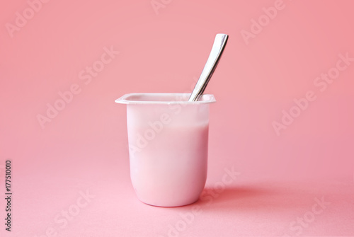 Delicious strawberry yogurt or pudding  in white plastic cup on pink background with copy space. Strawberry pink yoghurt with spoon in it. Minimal style. photo
