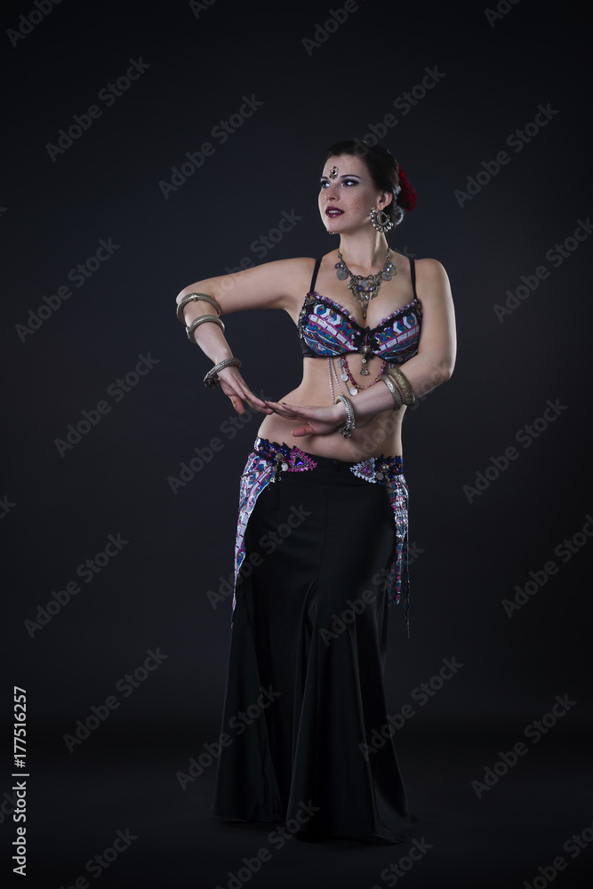 Women performs belly dance in ethnic dress on black background