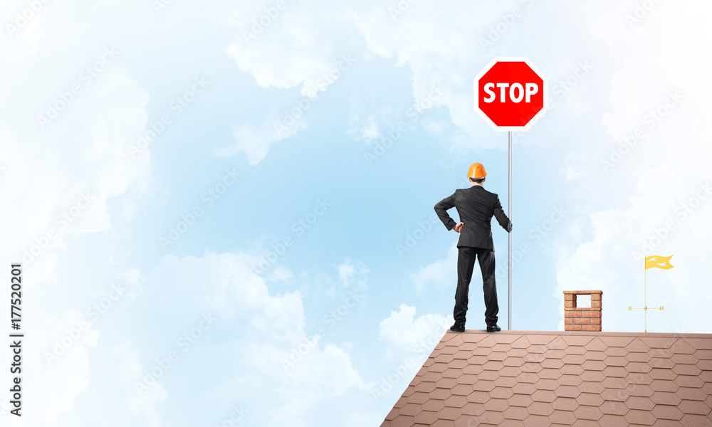 Caucasian businessman on brick house roof showing stop road sign. Mixed media Caucasian businessman on brick house roof showing stop road sign. Mixed media