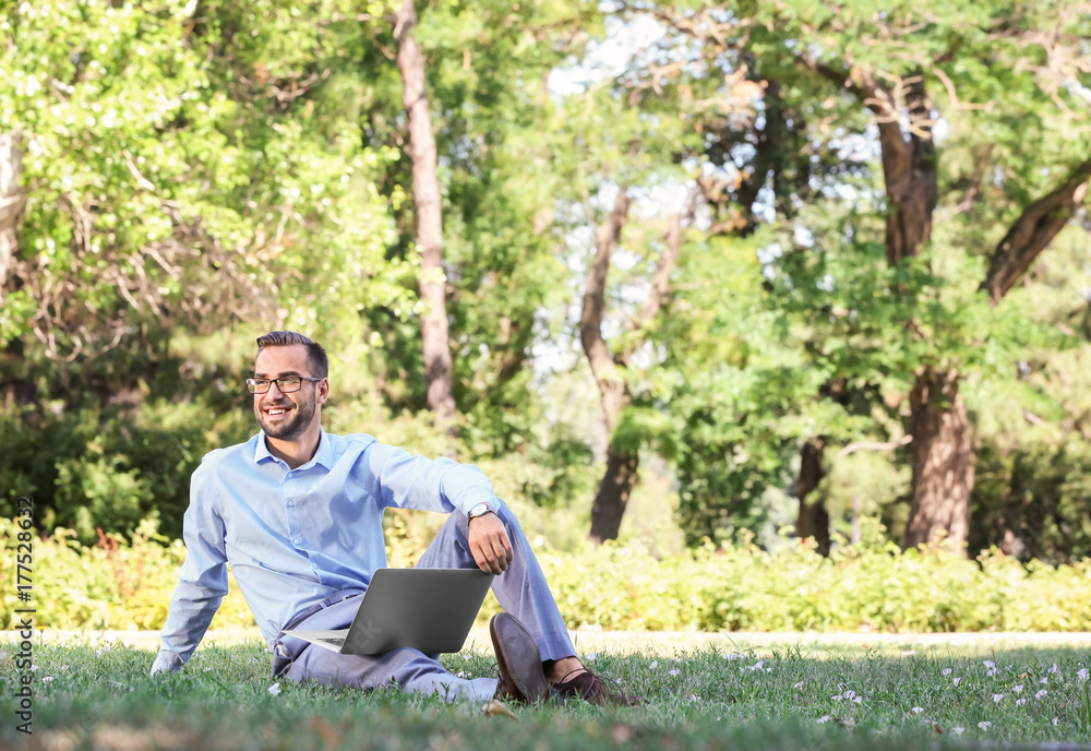 Obraz premium Elegant man with laptop sitting in park