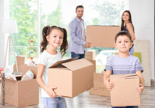 Cute little children with moving boxes in room at new home
