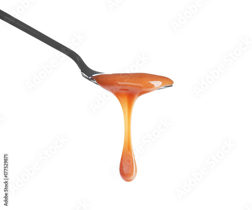Spoon with delicious caramel sauce on white background
