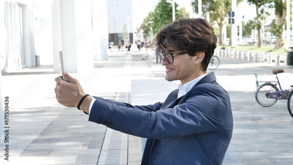 Handsome eleganty young business man wearing jacket sitting and working, looking down at a tablet computer that he is holding, outdoor Handsome eleganty young business man wearing jacket sitting and working, looking down at a tablet computer that he is holding, outdoor