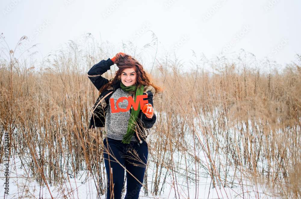 a young girl walks in the field. Dressed in winter clothes, she has blue eyes and thick red hair . Hair curls , the color of fire . The inscription love in the snow a young girl walks in the field. Dressed in winter clothes, she has blue eyes and thick red hair . Hair curls , the color of fire . The inscription love in the snow