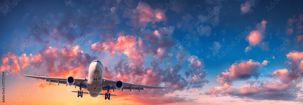Fototapeta premium Samolot i piękne niebo. Krajobraz z pasażerskim samolotem lata w niebieskim niebie z czerwonymi, purpurowymi i pomarańczowymi chmurami przy wschodem słońca. Podróżować. Samolot pasażerski. Samolot komercyjny. Prywatny odrzutowiec