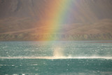 The sea is whipped up by strong winds underneath a rainbow.