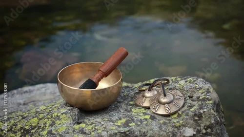 A Himalayan singing bowl on a boulder at a lake with calm water in the background photo