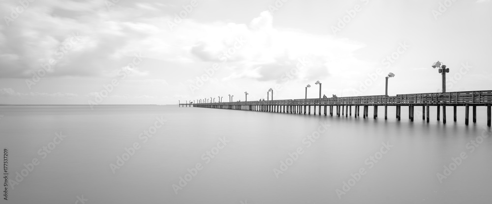 Naklejka premium Long exposure wooden fishing pier stretching out over Galveston Bay in La Porte, Texas, USA. Foot pier for saltwater fishing with motion blurred people, recreation concept. Panorama nature seascape