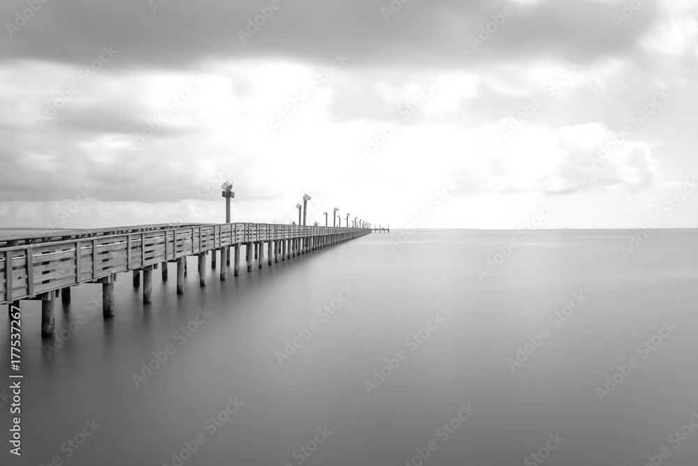 Obraz premium Long exposure wooden fishing pier stretching out over Galveston Bay in La Porte, Texas, USA. Foot pier for saltwater fishing with motion blurred people, recreation concept. Nature seascape background