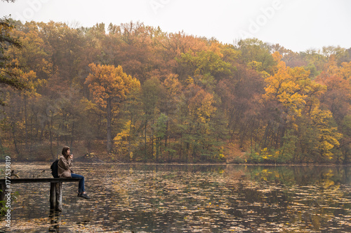 Young female hiker with backpack sitting at riverbank and looking at beautiful indian summer scenery. Young female hiker with backpack sitting at riverbank
