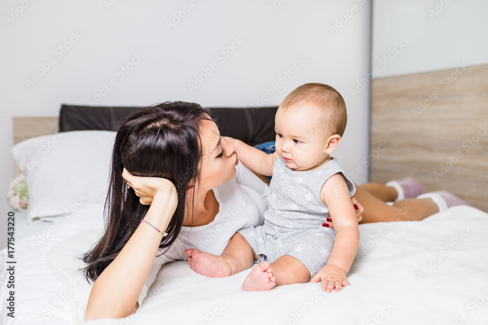 Beautiful mother enjoying and relaxing with her cute little baby on bed. 