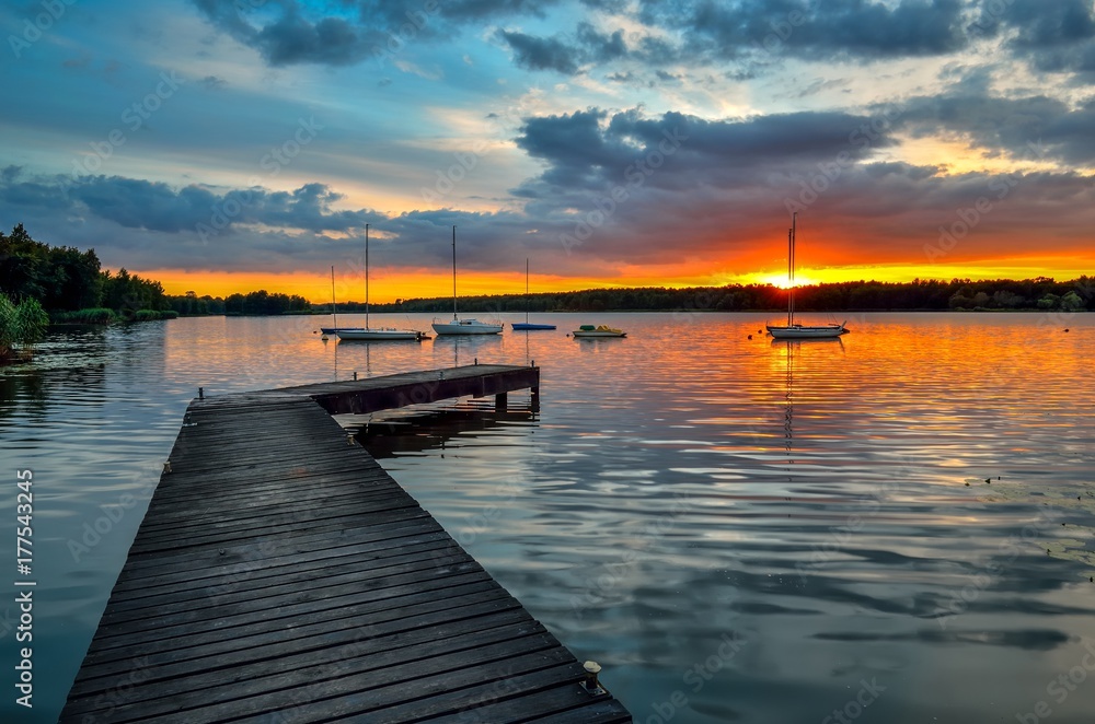 Beautiful summer evening landscape. Wooden pier and boat on the lake at sunset.