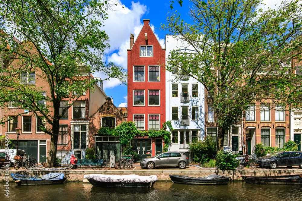 Traditional dutch houses and boats on canal in Amsterdam. Summer street. Urban landscape with typical old buildings, Netherlands, Europe.