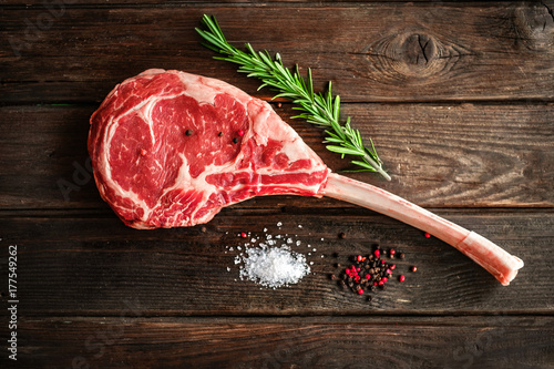 raw Tomahawk steak on wooden background with spices for grilling photo