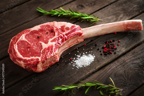 raw Tomahawk steak on wooden background with spices for grilling photo