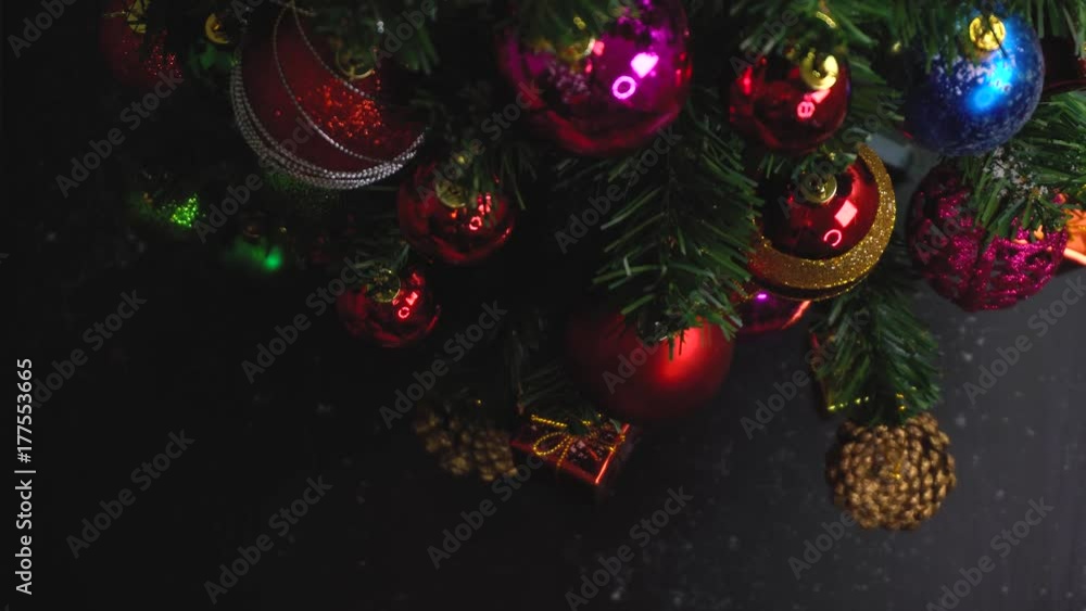 Greeting Season concept.Hand setting of Christmas tree and decorations with presents and ornaments on wood table from above with falling snow in 4k (UHD)
